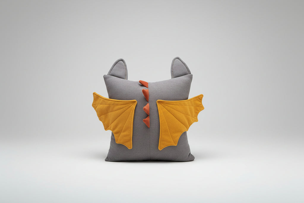 Gray pillow with dragon wings and tail on a brown couch against a light blue wall