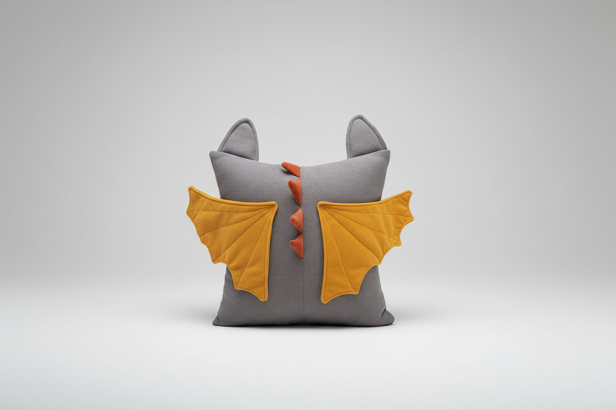 Gray pillow with dragon wings and tail on a brown couch against a light blue wall